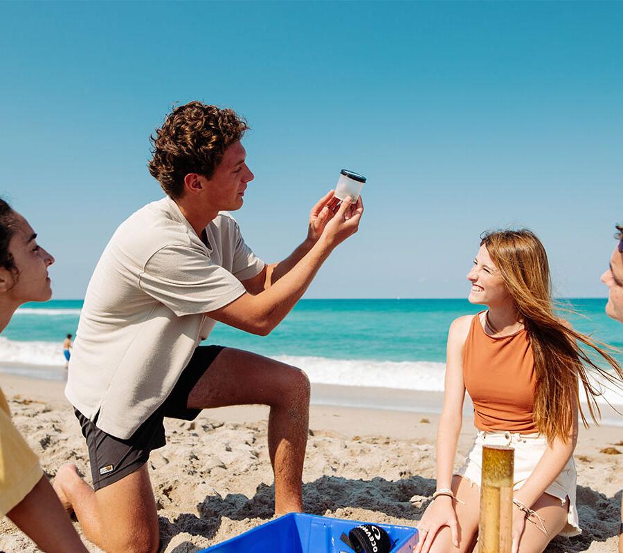 marine biology students at the beach looking at a jar of sand